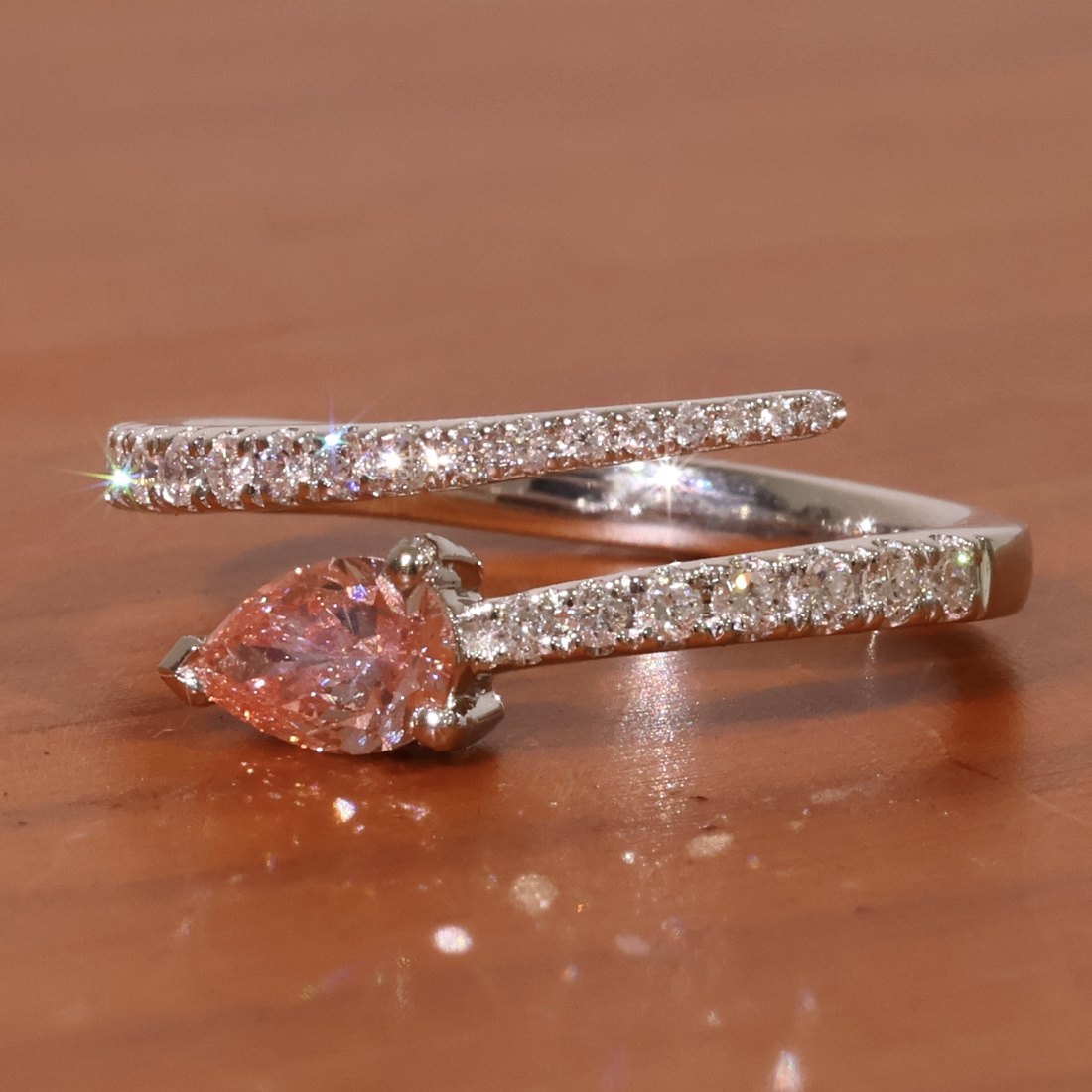 Pink pear cut diamond set in an open crossover ring with pave set diamond shoulders