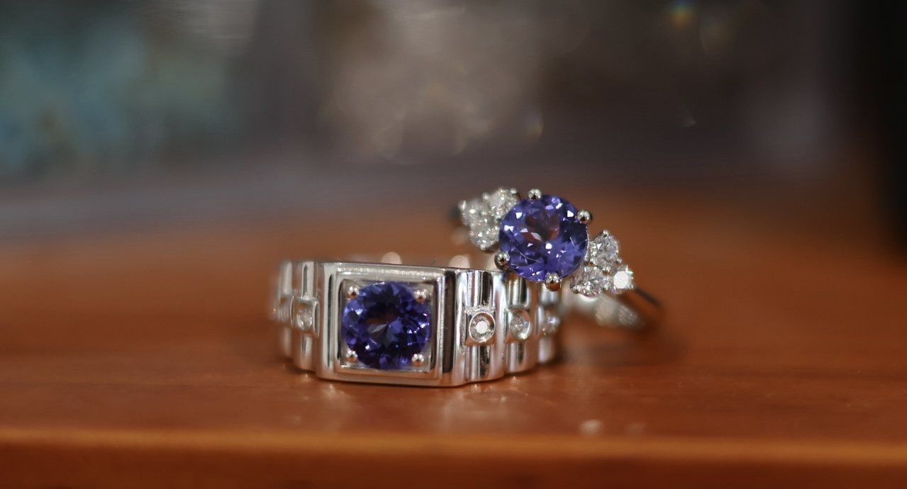 A matching pair of tanzanite rings, one in platinum with diamond shoulders and one in sterling silver, square set with diamond detail