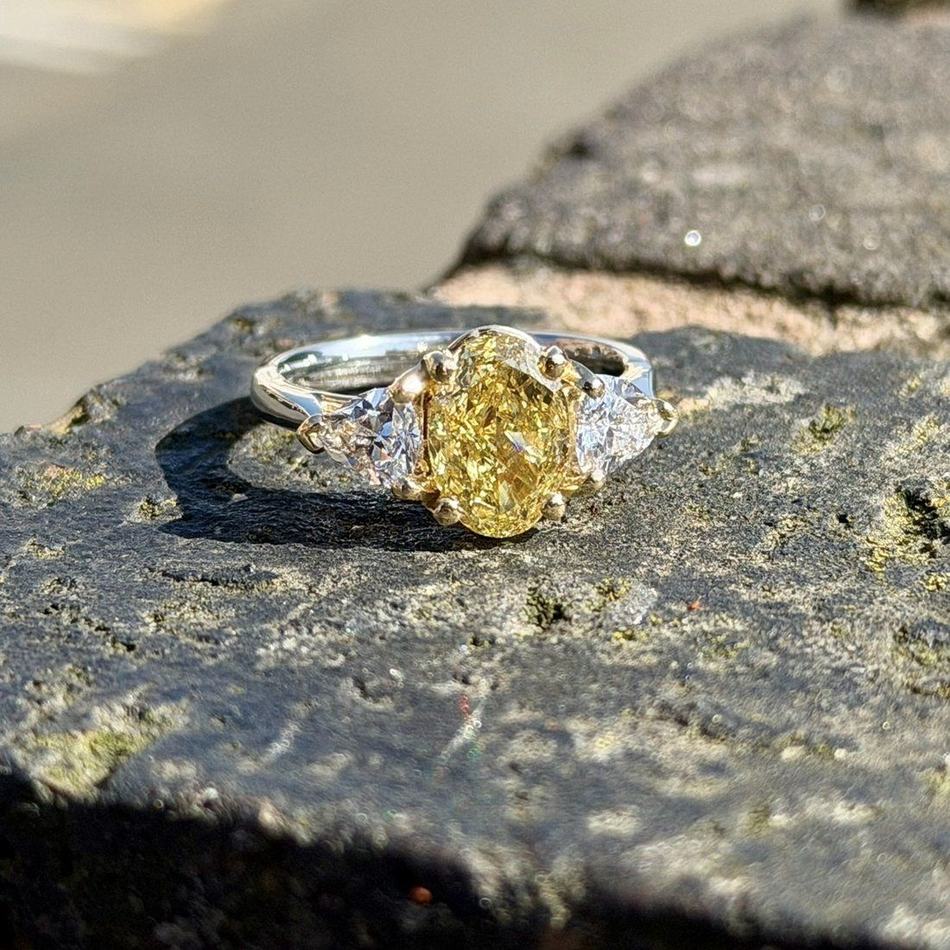 Fancy yellow oval cut diamond engagement ring with trilliant cut diamond shoulders, set in white metal